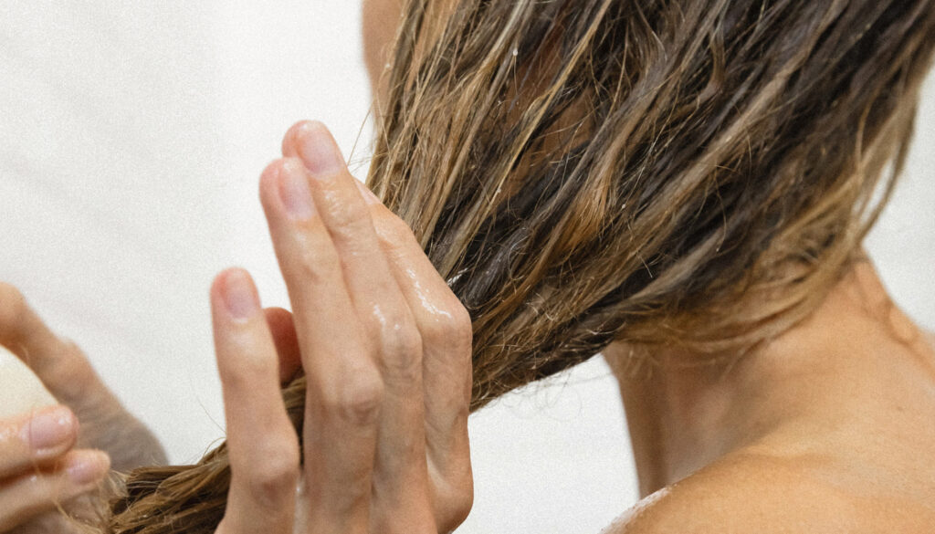 Kvinde med vådt hår påfører balsam i håret